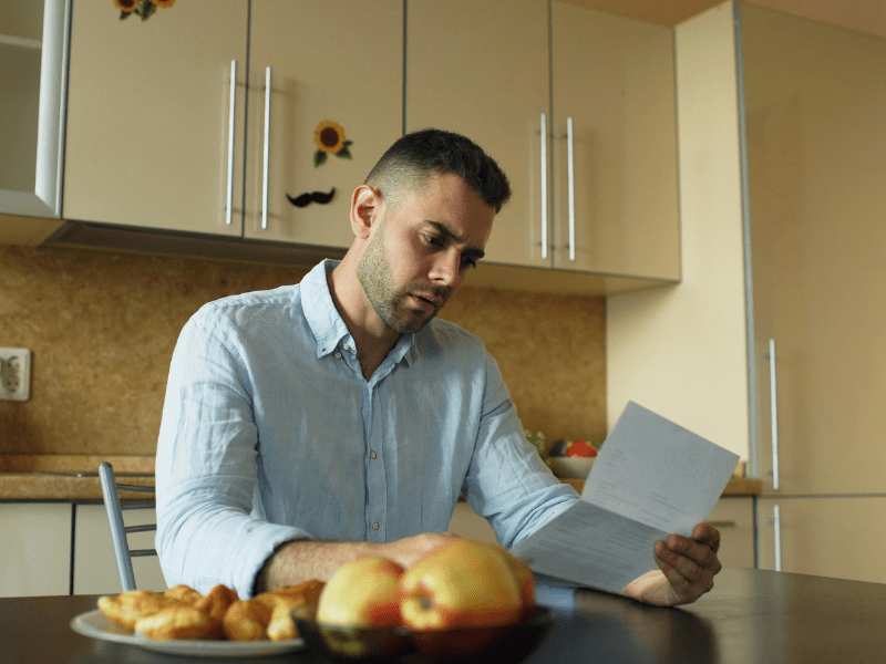 A man sitting at his kitchen table worriedly reading a garnishee notice sent by the ATO