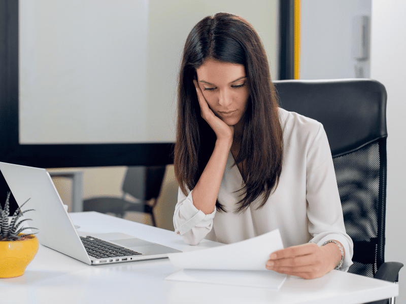 A woman resting her chin on her hand reads a document