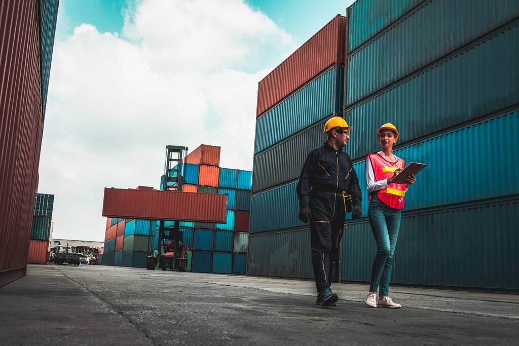 Two workers discussing supply chain issues regarding goods shipped in containers