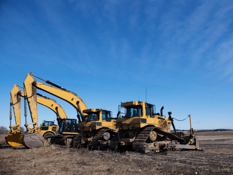 Several large yellow excavators parked at a construction site, striking blue skies in the background