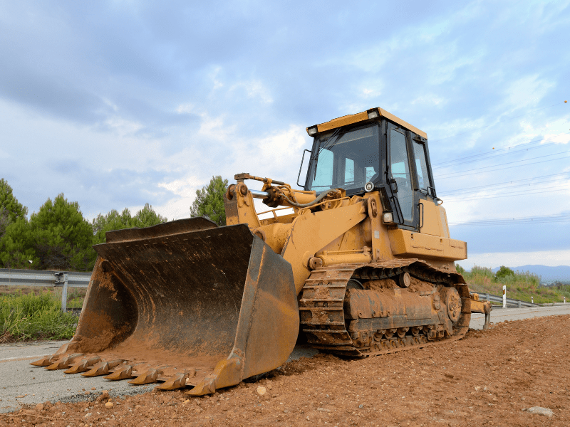 A large yellow bulldozer on the road, red soil underneath