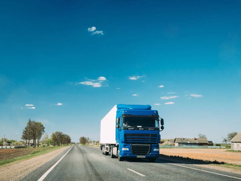 A blue prime mover driving down a rural road, blue skies in the background