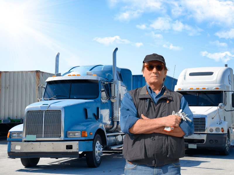 A trucking business owner poses in front of two freight trucks