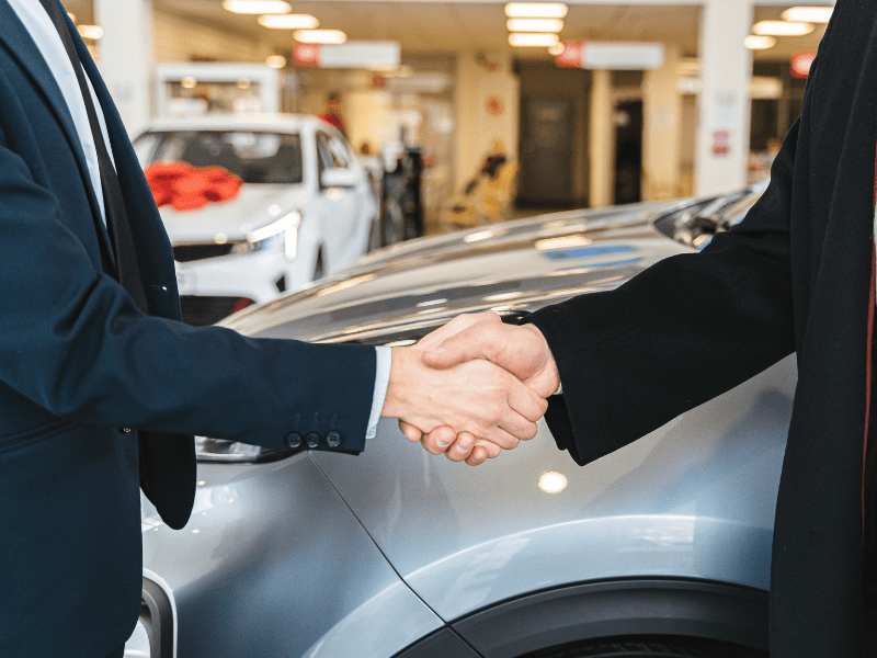 A car salesman and a customer shake hands at a car dealership