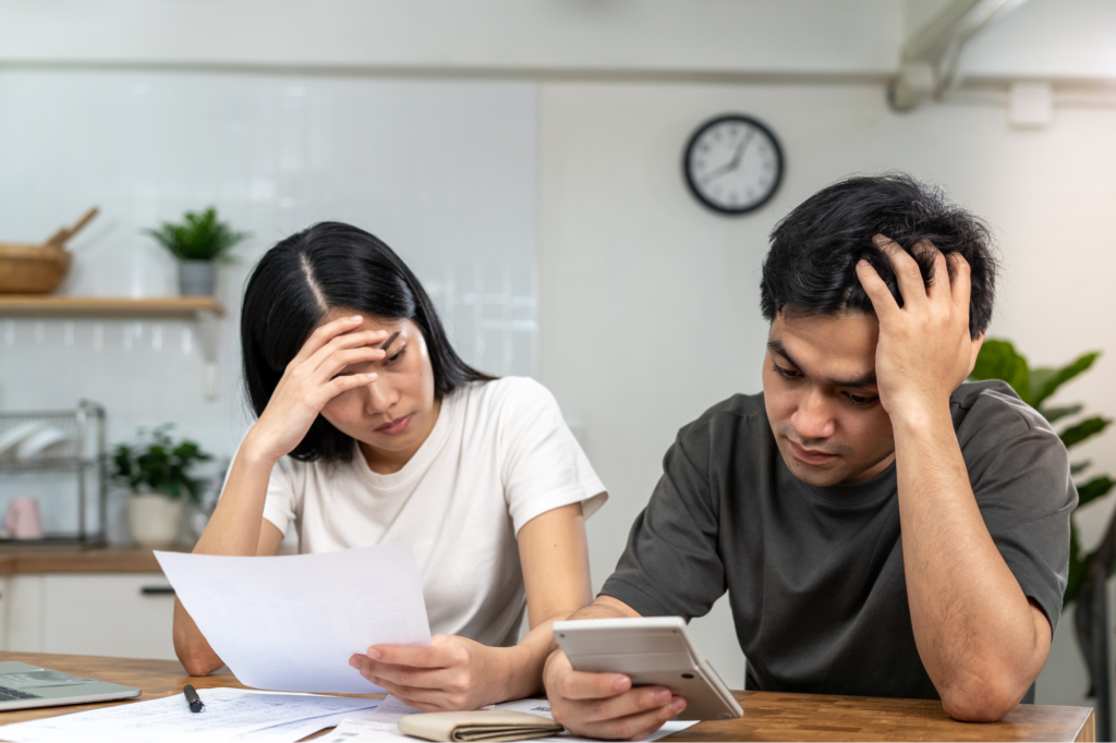 Young business-owning couple looking stressed, calculating tax debt, man holding and looking at a calculator, woman holding a document, concept photo for experiencing tax debts and needing tax debt loans