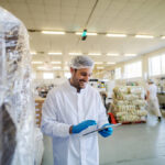 Young male manager in standing in food factory and looking at tablet.