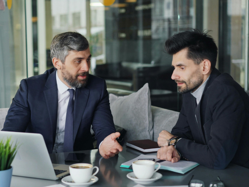 Two business partners talk about a potential partner buyout, two men in suits in a discussion over coffee