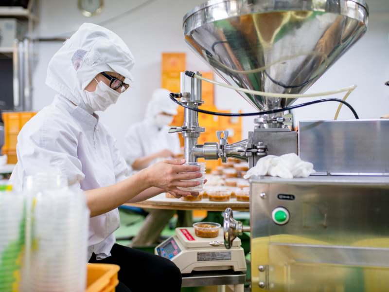 Factory workers in a food factory packaging food into containers, wearing food safety apparel