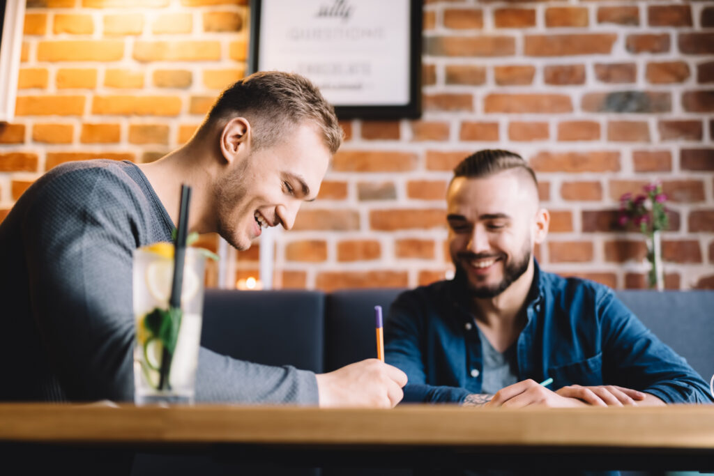 Two adult men sitting on a booth table at a restaurant, cheerful, writing, discussing business in an informal setting