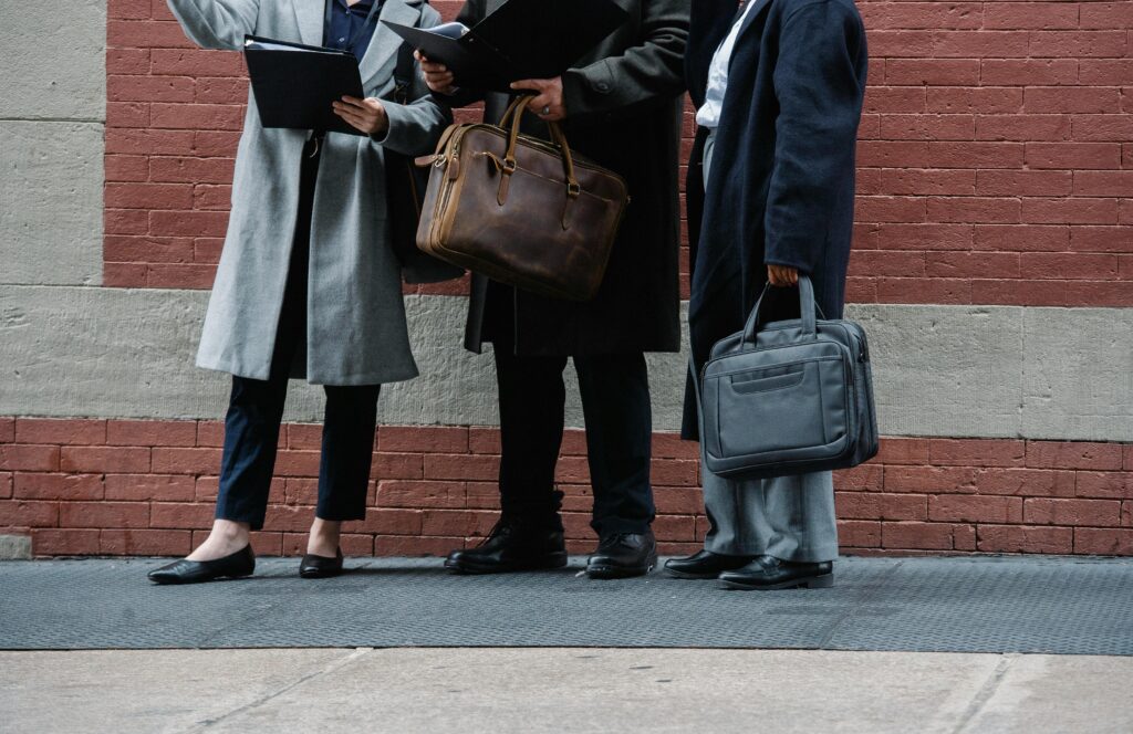 Cropped photo of three professionals, dressed in business attire, standing by the sidewalk, discussing finance, holding folders and papers