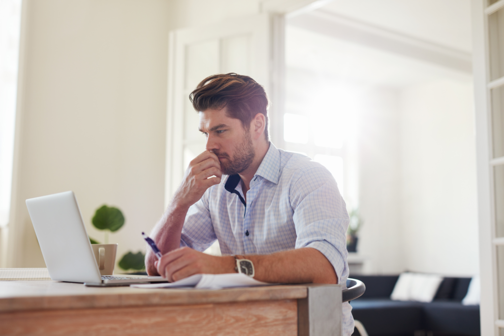 Man in a brightly lit room reading the screen of his laptop looking mildly stressed, concept photo for business owner in tax debt with the ATO