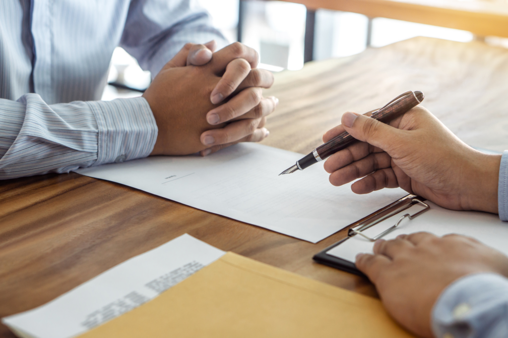 Cropped photo of two men seated across each other at a table with one man filling out documents with a fountain pen. Concept photo for applying for a tax debt loan.