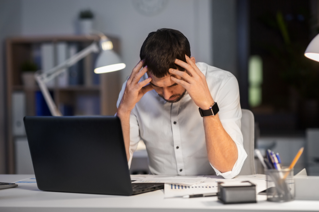 Man holding his head in his hands, stressed man reading documents while seated at his work table, concept photo for man in tax debt trouble with the ATO