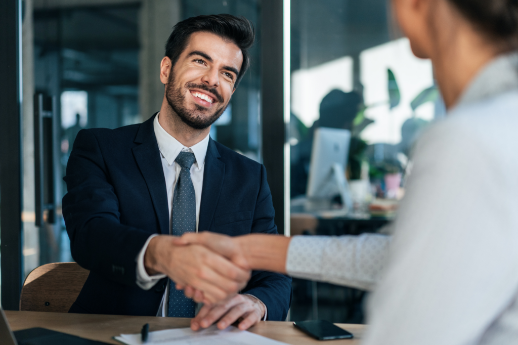 A man in a suit happily shakes hands with a woman seated across him, concept photo for a business owner getting an unsecured business loan approved