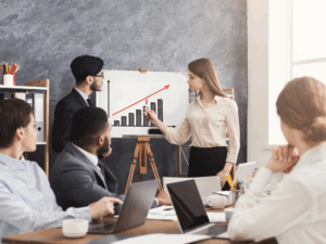 A company meeting where a man and a woman present a rising graph that represents the company’s profits