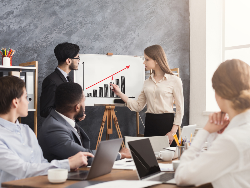 A company meeting where a man and a woman present a rising graph that represents the company’s profits