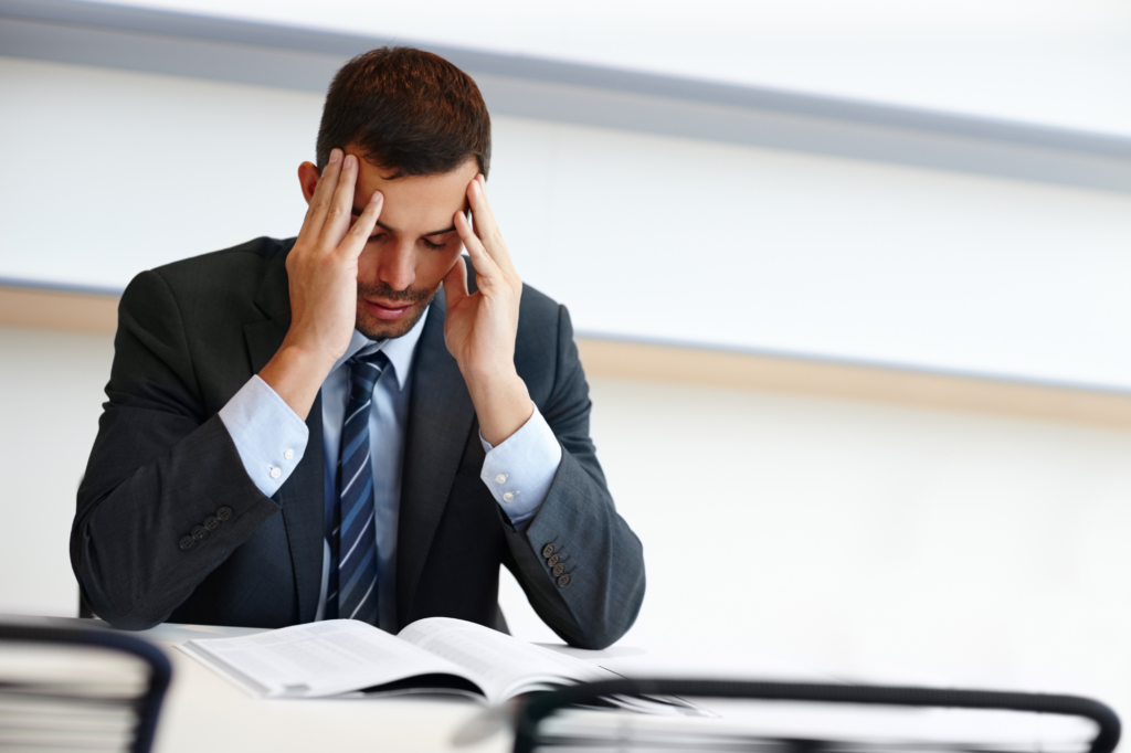 Man in a suit holds his temples with his eyes closed, stressed after reading document, concept photo of a businessman after receiving a notice to complete