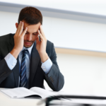 Man in a suit holds his temples with his eyes closed, stressed after reading document, concept photo of a businessman after receiving a notice to complete