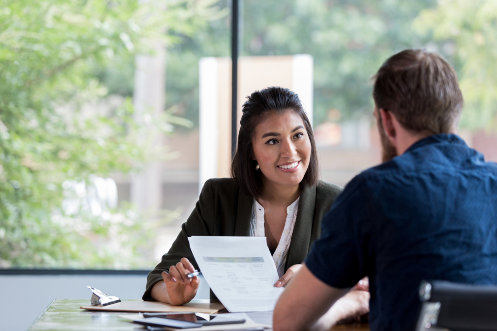 A woman holding documents seated across a man smiles, explaining second mortgage loan terms to a business owner