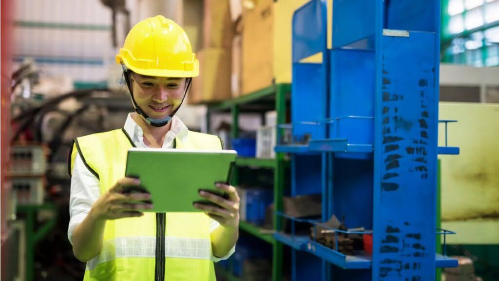 Factory worker in a hi-vis vest and hard hat happily reads something on an electronic tablet. Concept photo of using tax debt loans like equipment finance to pay off tax debt.