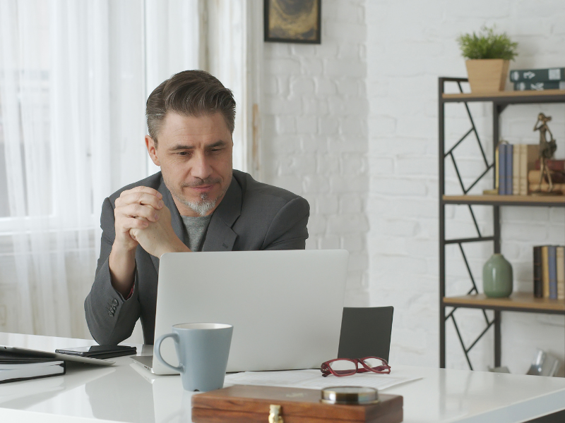 A business owner clasps his hands together as he looks at the screen of his laptop, considering an unsecured loan for his business.