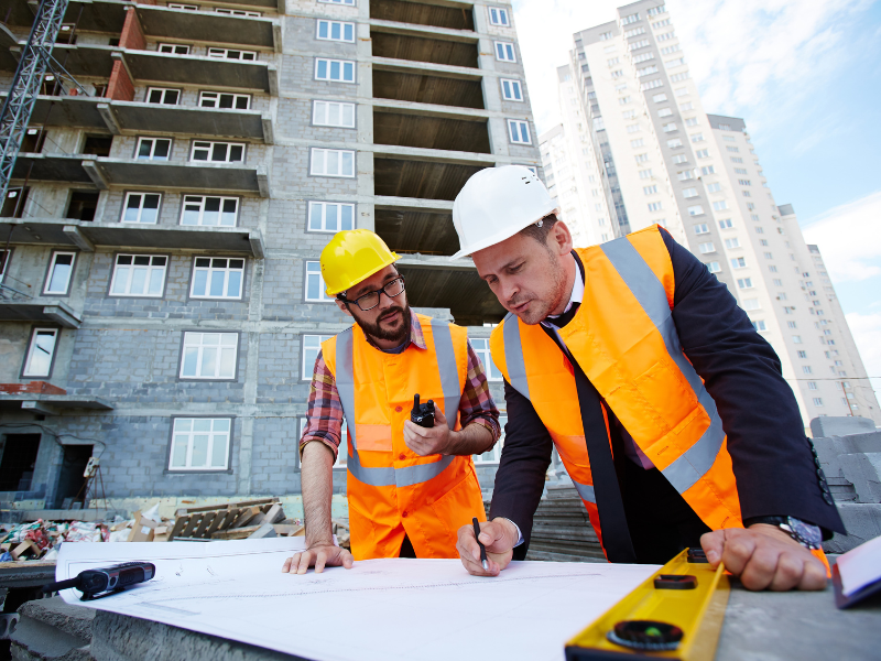 Two engineers discuss and edit plans at an ongoing construction site