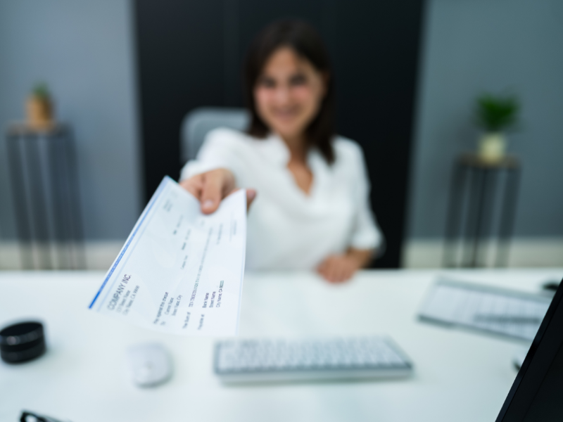 A woman handing a paycheck towards the camera