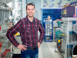 A business owner in plaid poses inside his hardware store