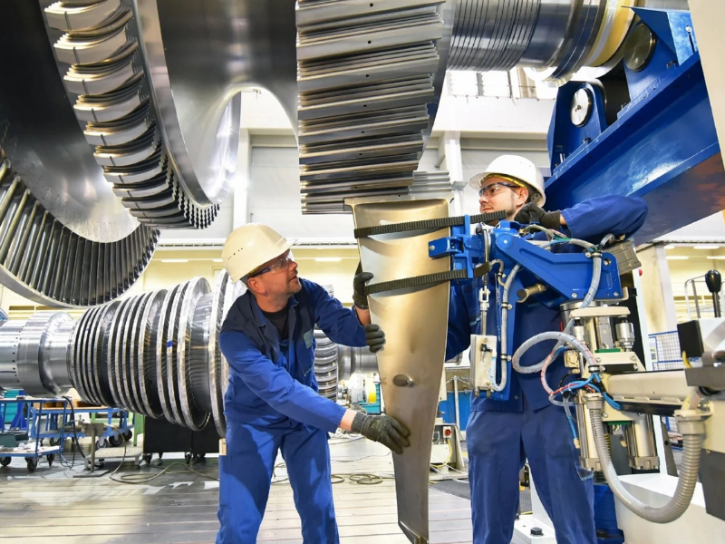 Two workers in protective uniforms work inside a manufacturing plant