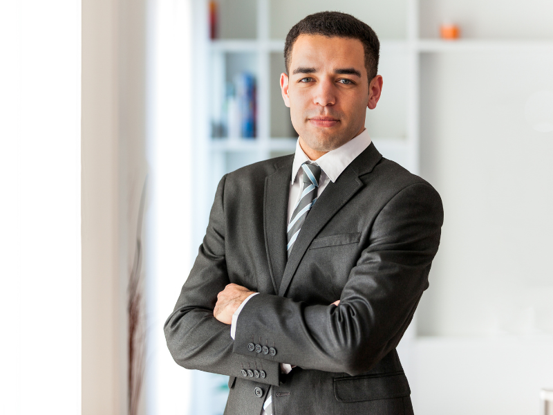 A business owner in a suit crosses his arms and slightly smiles at the camera