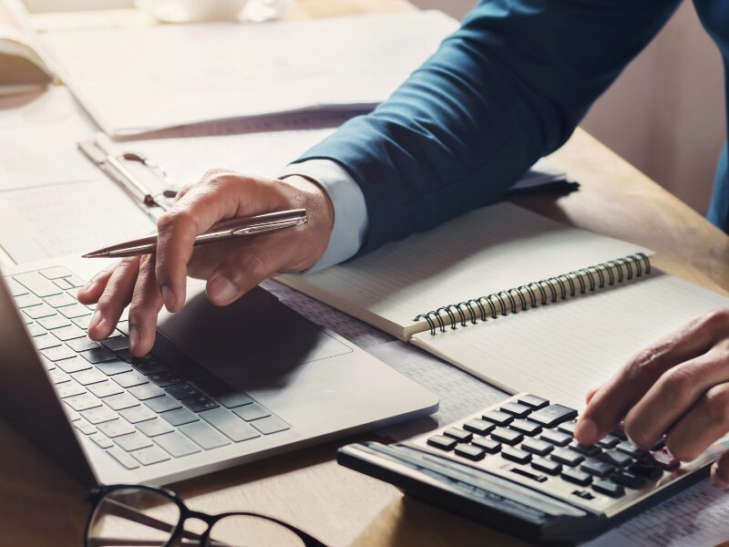 A man’s hands typing on a laptop while using a calculator, a business owner monitoring business finances