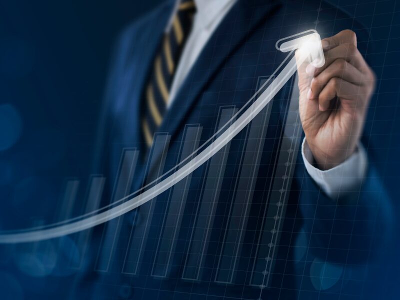 A businessman doing a writing gesture, with a graphic of a rising bar graph with an upward arrow, concept photo for business growth