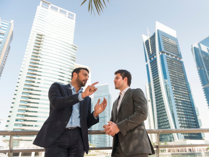 Two businessmen discuss growth strategies outdoors in the city, with tall buildings in the background
