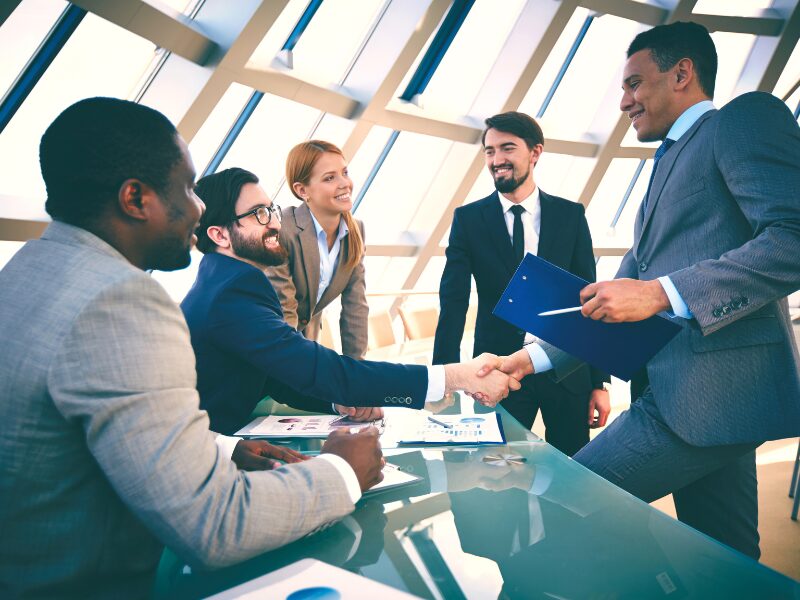 Employees of a business in a meeting, with the business owner shaking hands with a client