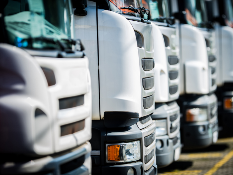The fronts of several white freight trucks parked in a row at a facility
