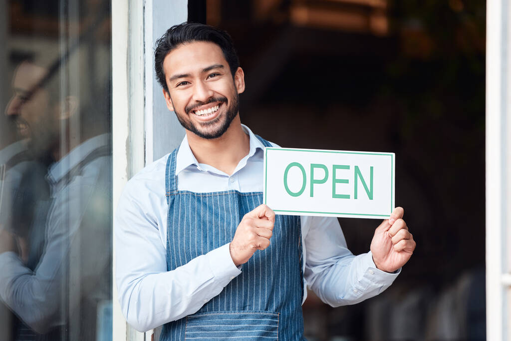 Happy asian man, small business and portrait with open sign for service in coffee shop or restaurant. Male entrepreneur, manager or waiter holding billboard or poster for opening retail store or cafe