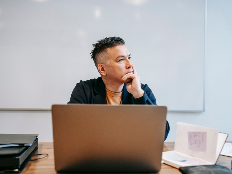 A man seated in front of his laptop looking to his left deep in thought