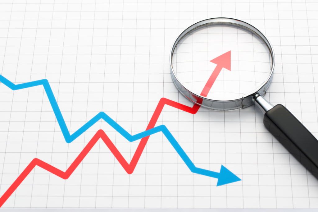 Two lines on a graph, one in red, rising, representing the rise in wages. One line in blue, falling, representing profits. A magnifying glass focuses on the red line, highlighting the rise of salaries and wages.