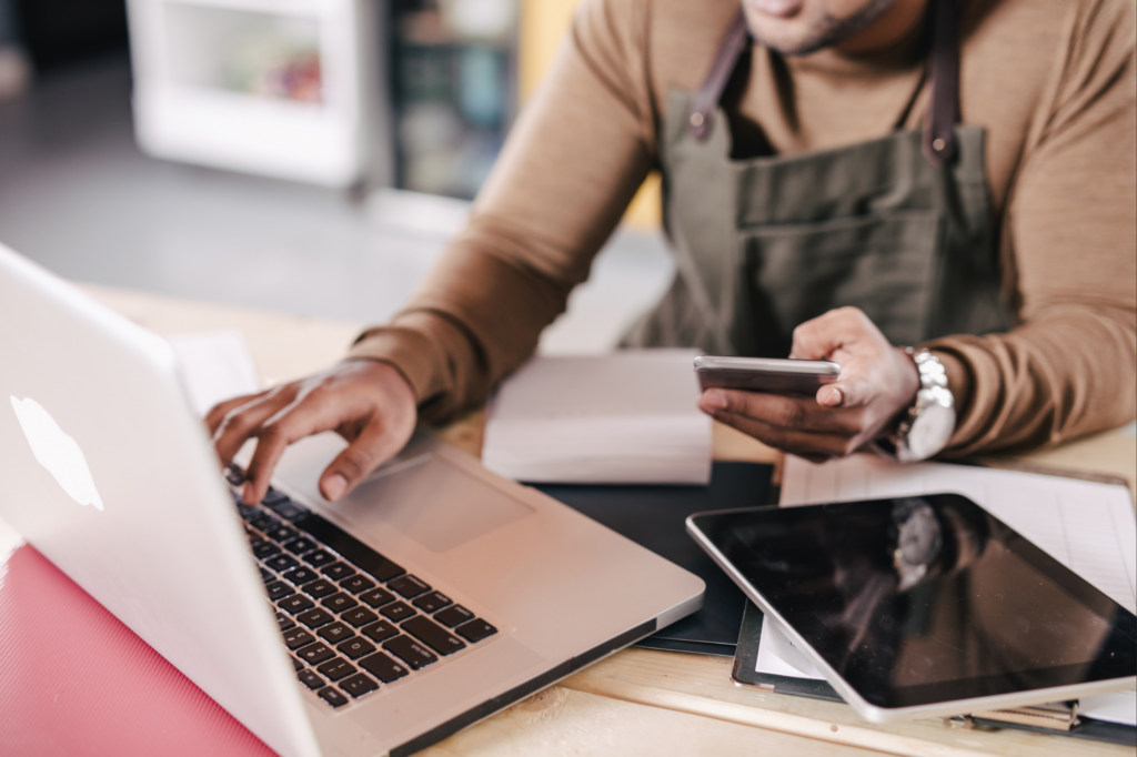 Small business owner applying for business line of credit, applying for loan, cropped photo of man holding phone and reading laptop screen, electronic tablet and papers visible on table