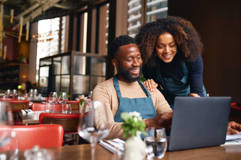 A couple that owns a small business smiles as they read laptop screen, loan approval, concept photo