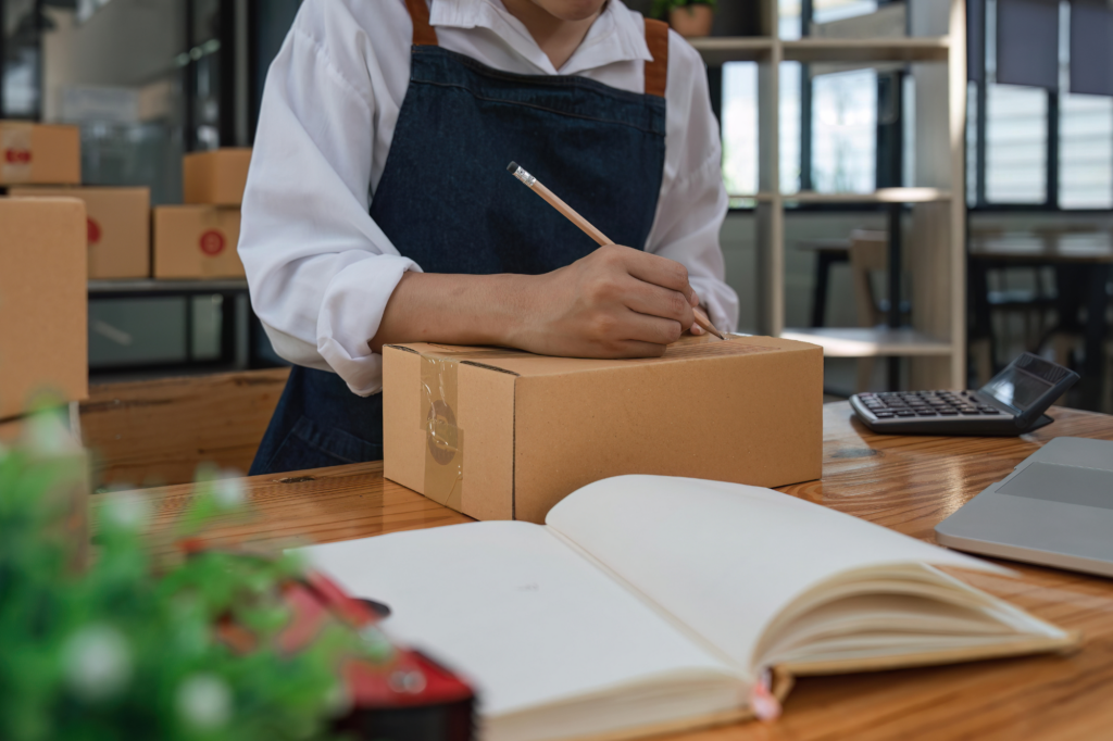 Small retail business owner boxing orders, cropped photo, man in long sleeve white shirt and denim apron