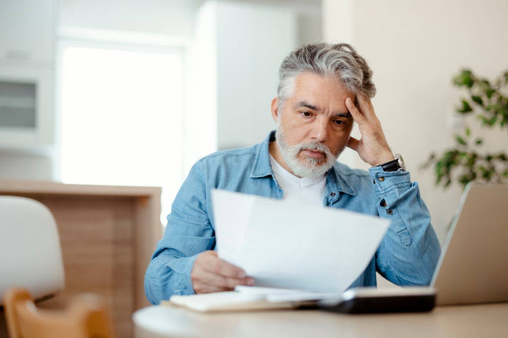 Older man stressed reading document, hand holding his temple, business owner receiving ATO Director Penalty Notice