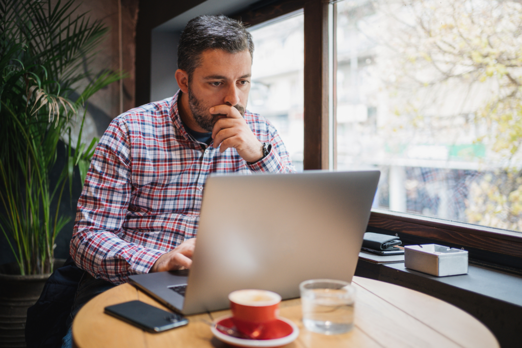 business owner sitting at a cafe, looking intently at his laptop, business recovery from tax debt, business restructure