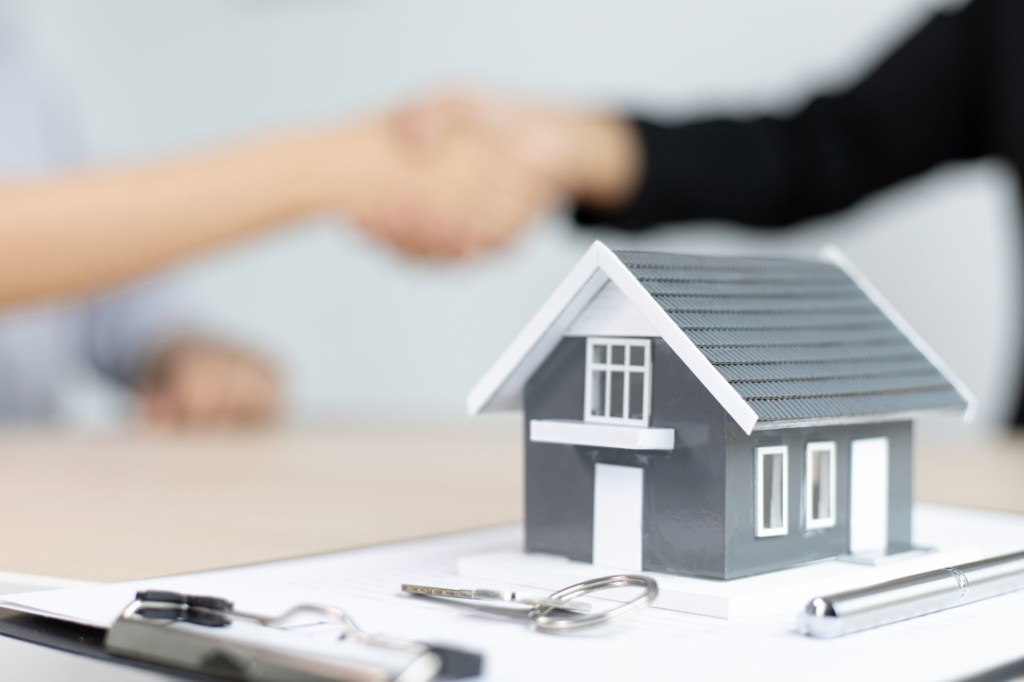 Model minature house, clipboard, and keys in the foreground, a handshake in the background, blurred, concept photo for an SMSF loan being approved