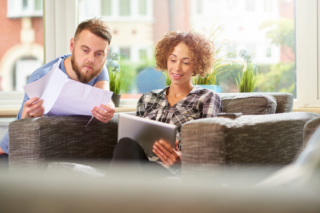 A couple sitting in their brightly lit living room, the man reading documents and the woman looking at an electronic tablet, they're in a good mood, loan approval