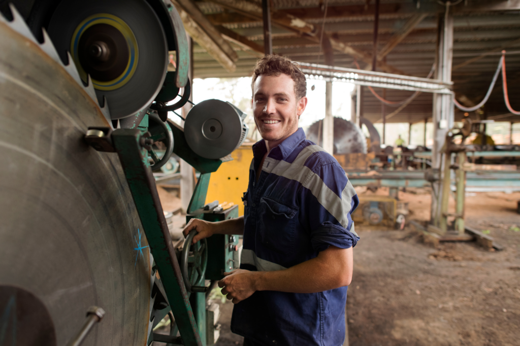 Factory worker smiles at camera as he operates plant machinery, photo of worker inside factory, concept photo of using plant equipment for asset based loans in Australia