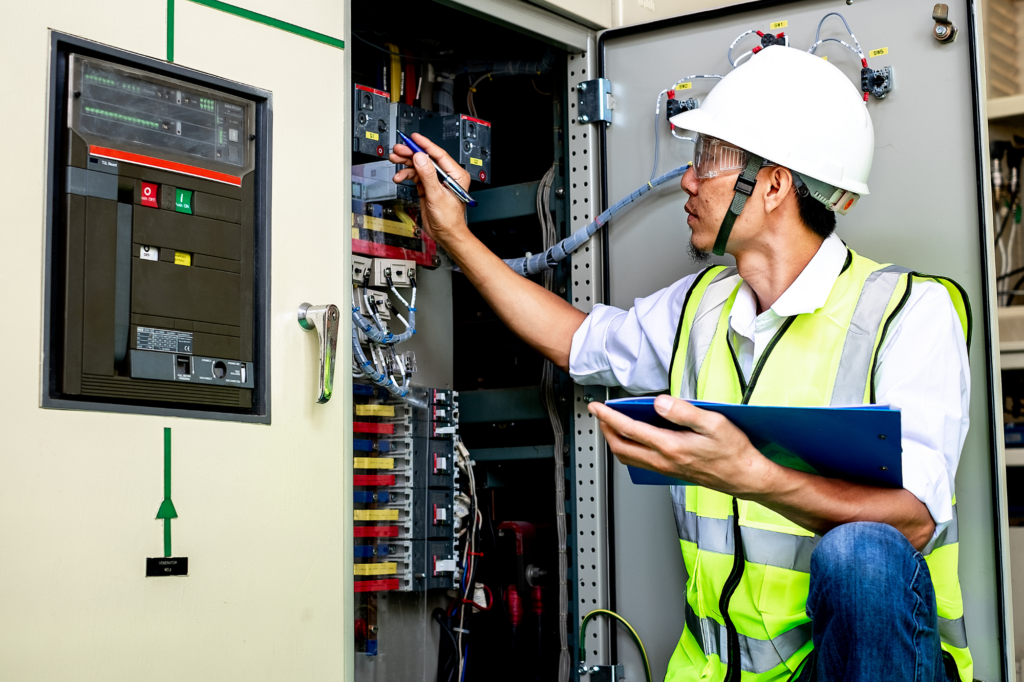 Electrical and data contractor wearing a hard hat and hi-visibility vest, holding a clipboard and checking data wiring