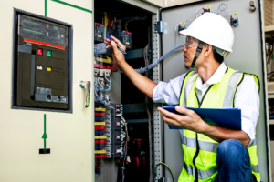 Electrical and data contractor wearing a hard hat and hi-visibility vest, holding a clipboard and checking data wiring