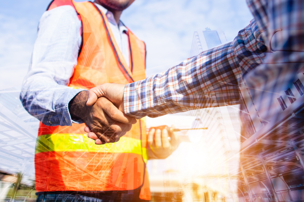 Electrical engineer in hi-visibility vest shakes hand with client in atmospheric photo with overlay of a cityscape