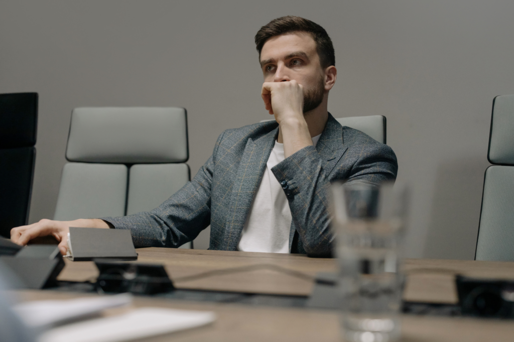 Photo of a stressed looking man, businessman in debt or bankruptcy, man in semi-formal clothing sitting at a conference table looking at the distance